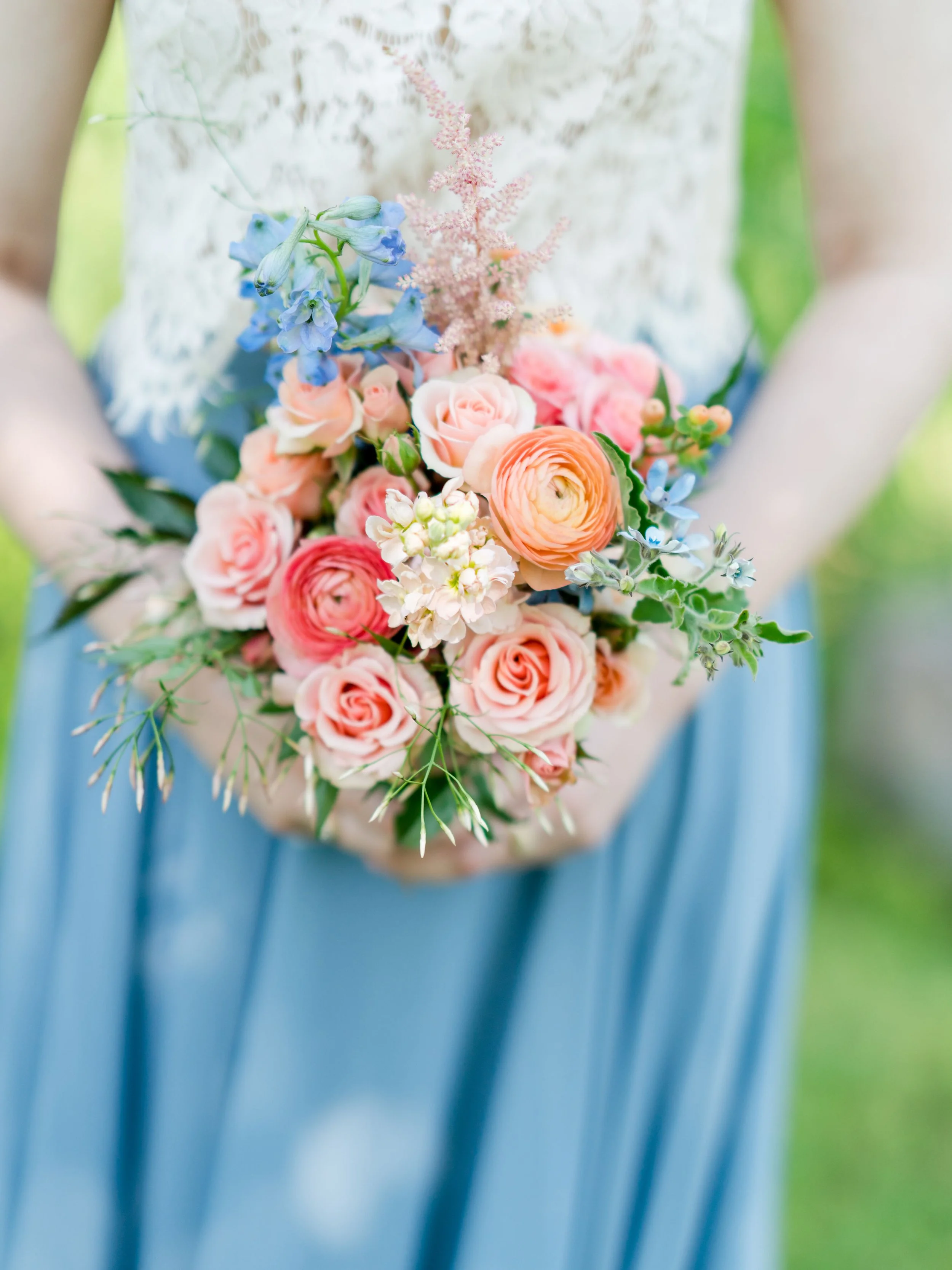 A person in a blue dress holding a bouquet of pink, peach, and blue flowers with greenery.