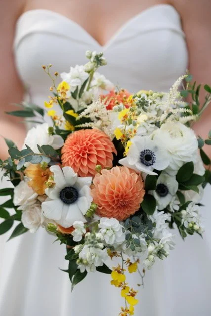 Bride holding a bouquet of white, orange, and yellow flowers with greenery.