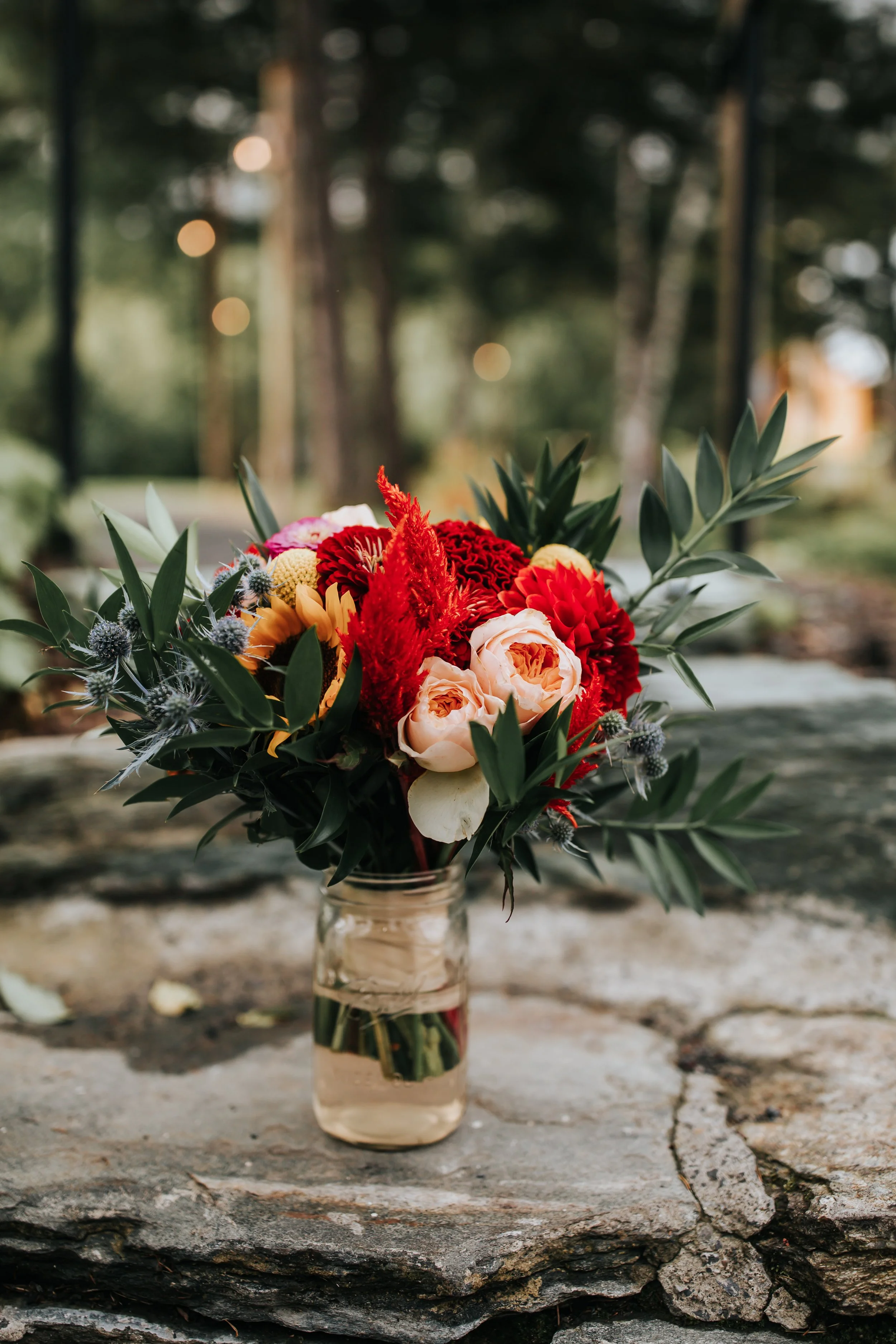 A colorful floral bouquet in a glass vase on a rustic wooden surface outdoors.