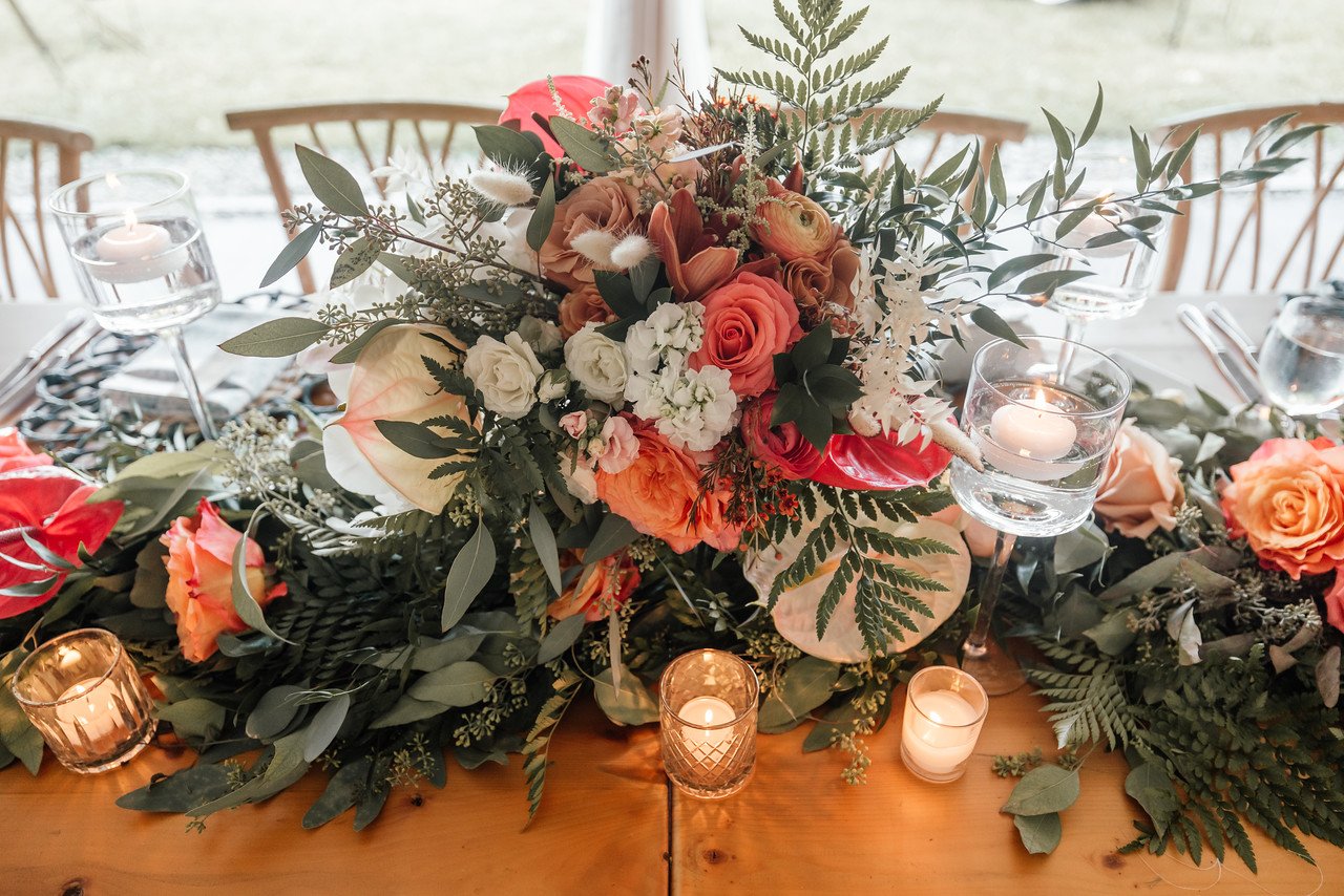 A floral centerpiece on a table with candles, surrounded by chairs and tableware, at a decorated event or wedding.