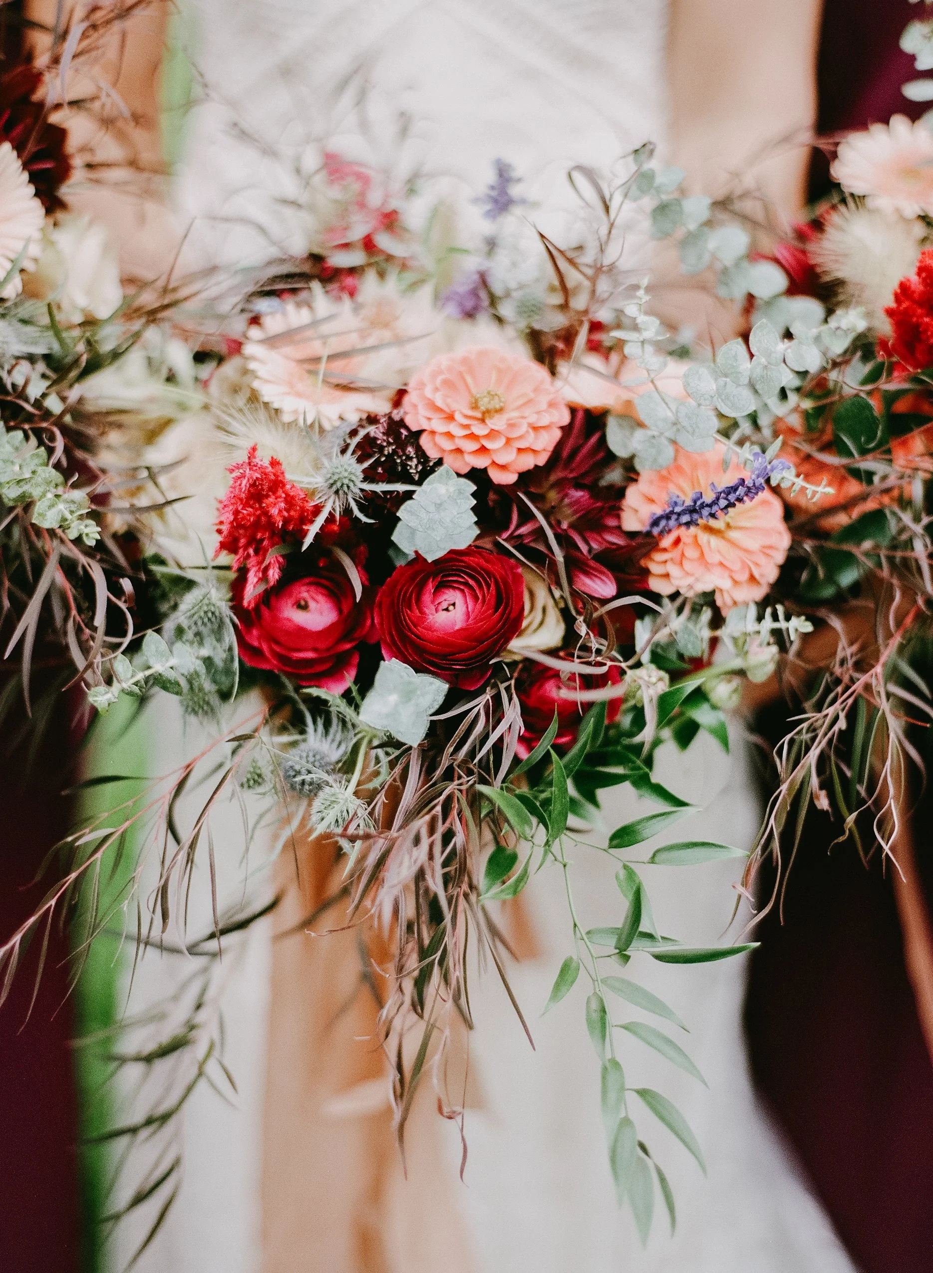 A bouquet of various flowers including pink, red, purple, and white blossoms with green and silver eucalyptus leaves. The background is blurred.