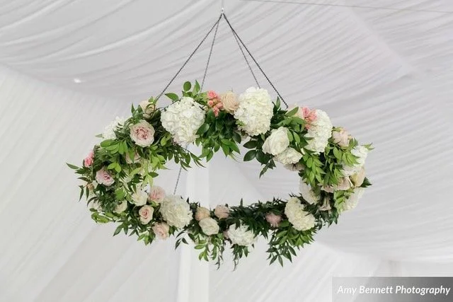 A floral wreath with white and pink flowers and green leaves hanging from the ceiling.