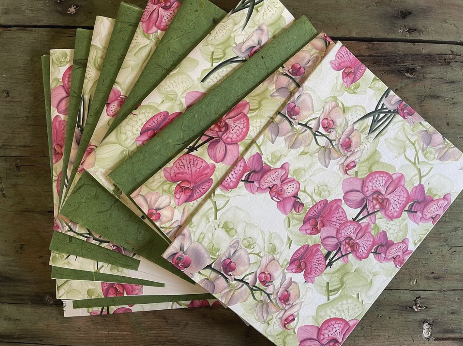 Multiple sheets of floral wrapping paper with pink and white orchids, partially unrolled on a wooden surface.