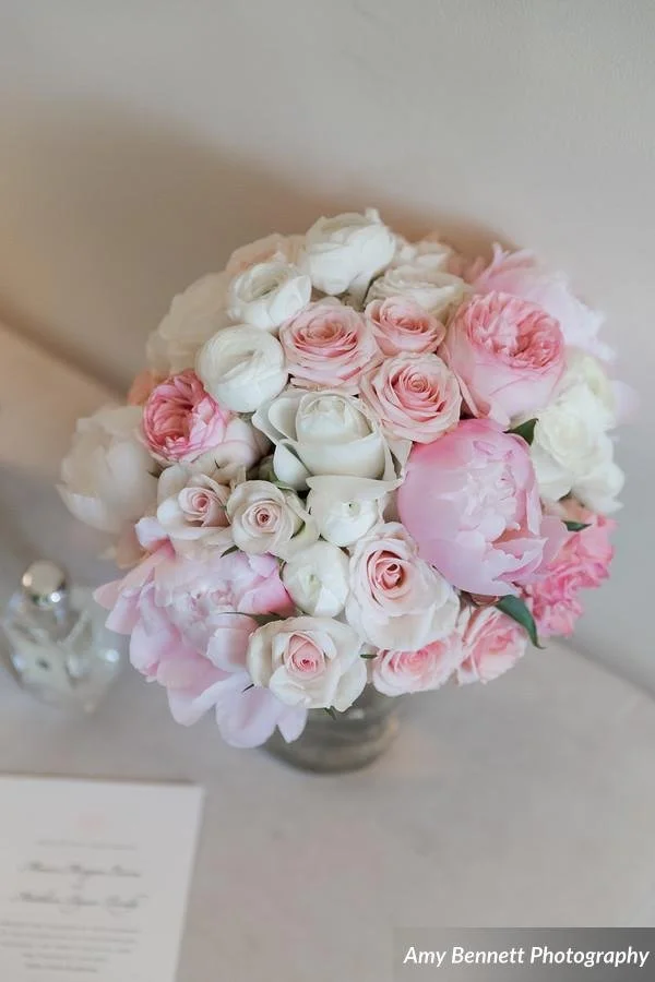 A bouquet of pink and white roses and peonies in a vase on a table.
