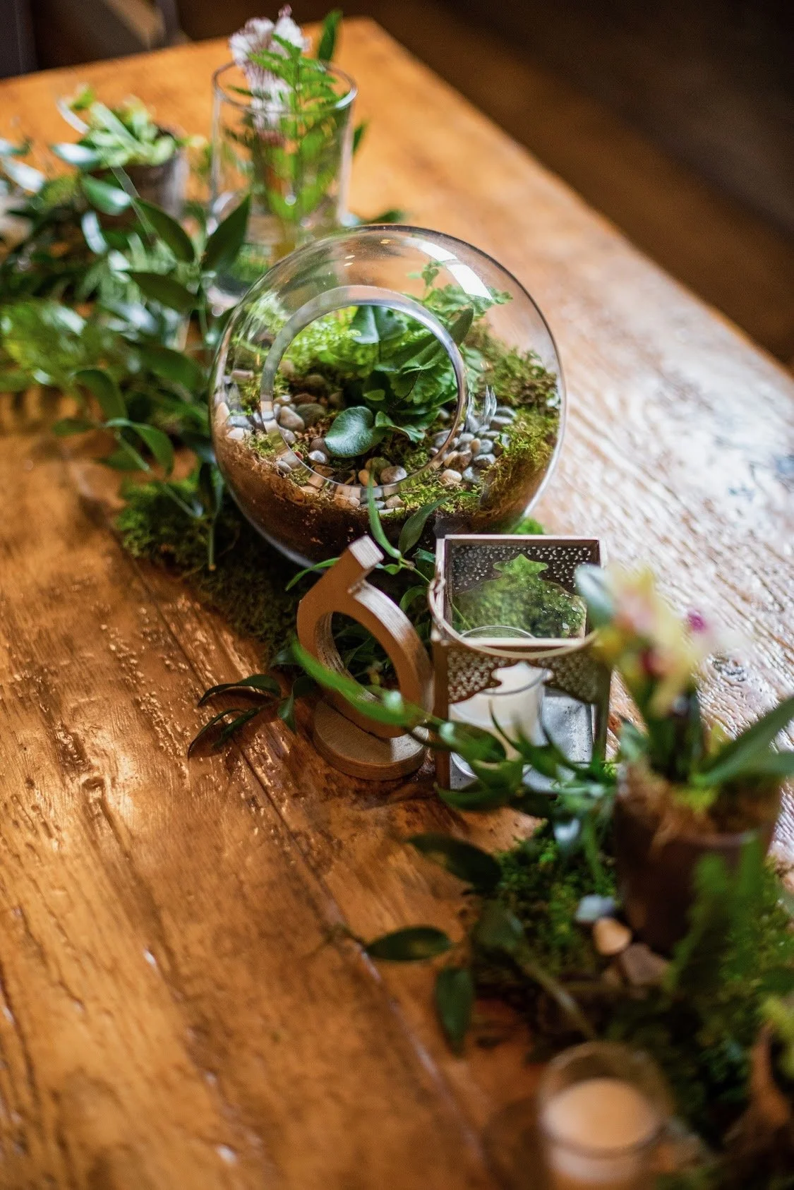 Decorative glass terrarium with plants and pebbles on a wooden table.