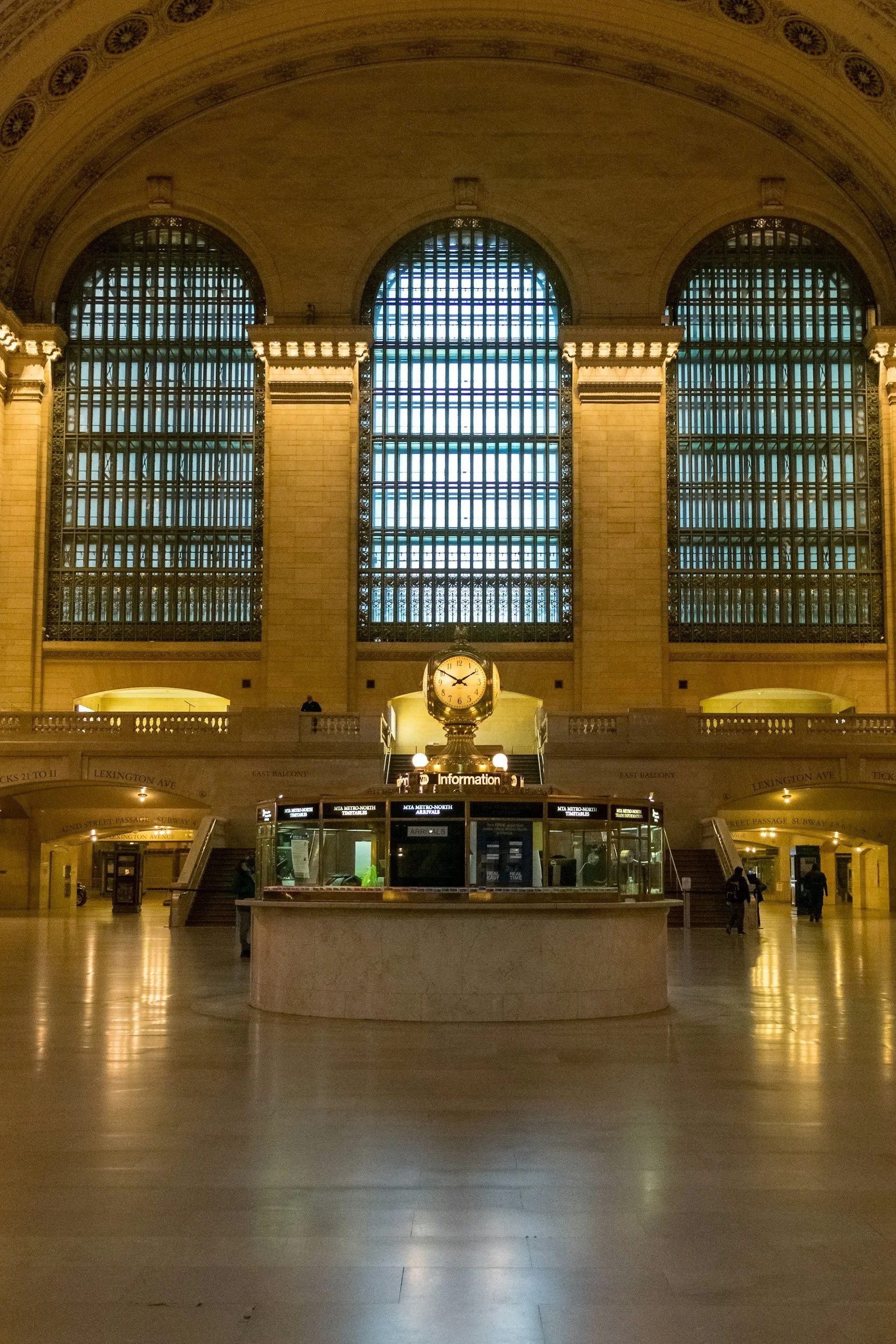 Inside Grand Central Terminal showing large arched windows, a clock, and a ticket kiosk in the center.