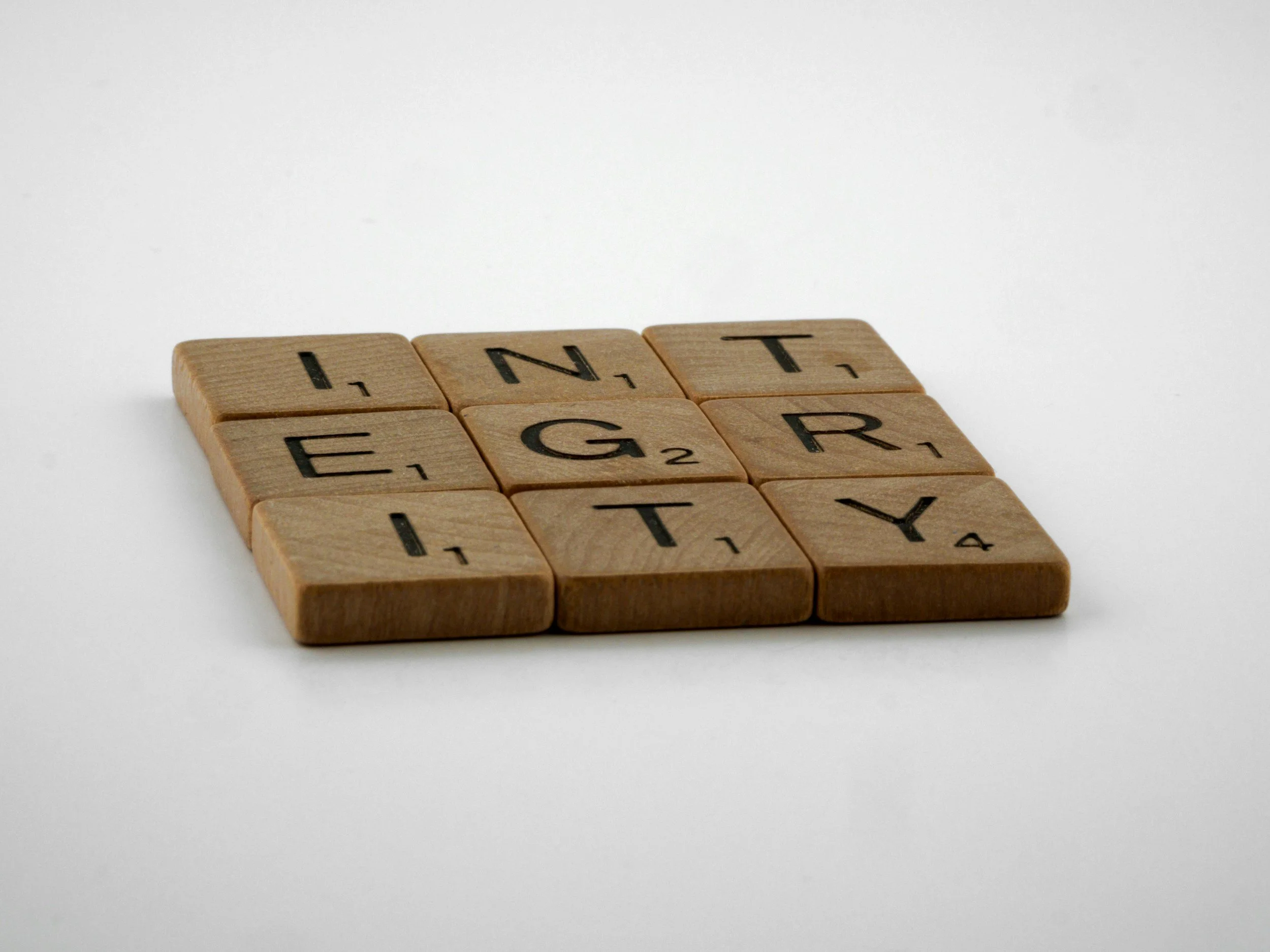 A group of tan wooden Scrabble tiles spelling out the letters 'I,' 'N,' 'T,' 'E,' 'G,' 'R,' 'A,' 'T,' 'E' on a white background.