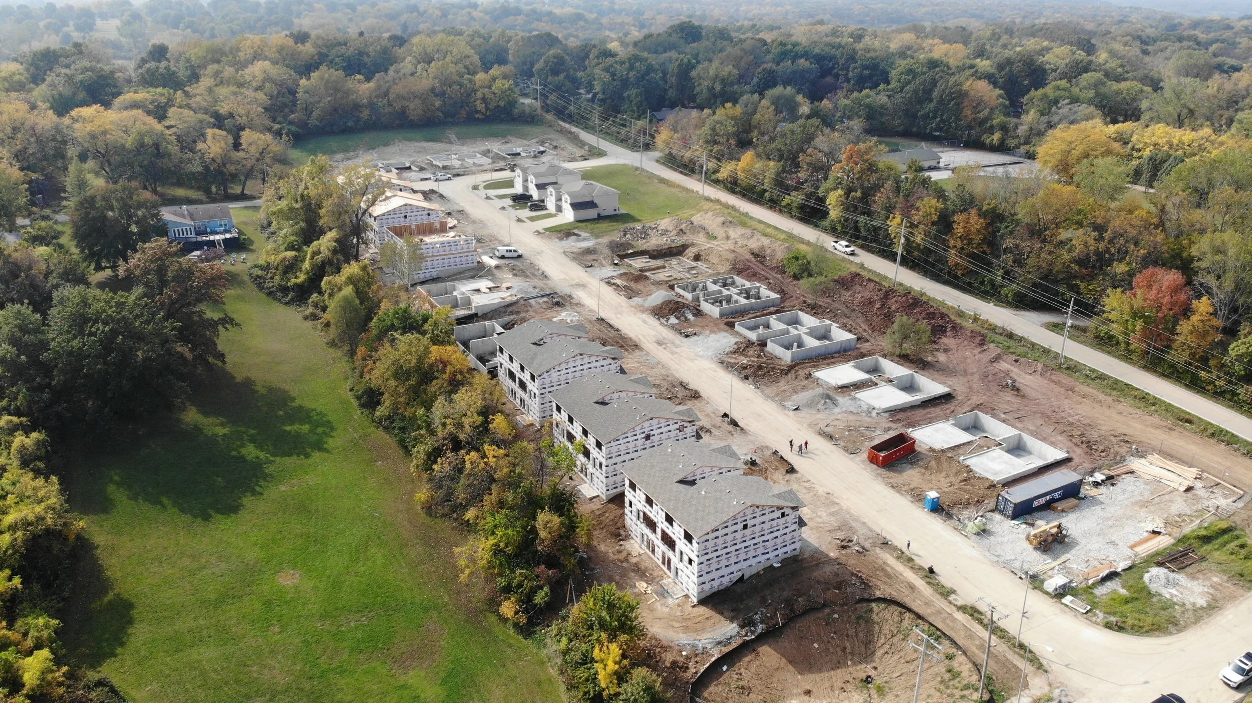 Aerial view of a construction site with multiple under-construction buildings, surrounded by trees and greenery.