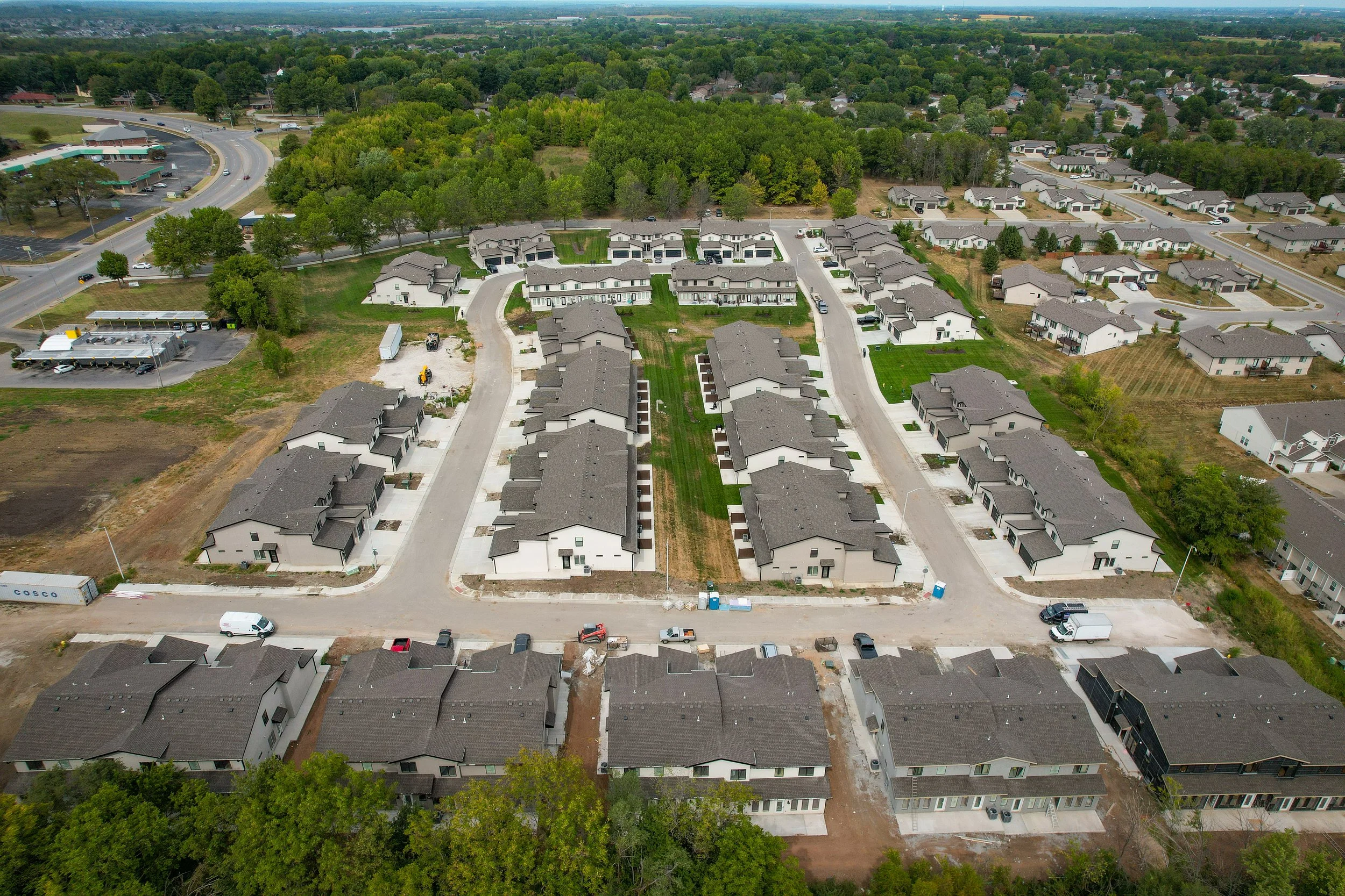 Aerial view of a residential neighborhood with newly built townhouses, surrounding greenery, and some undeveloped land.