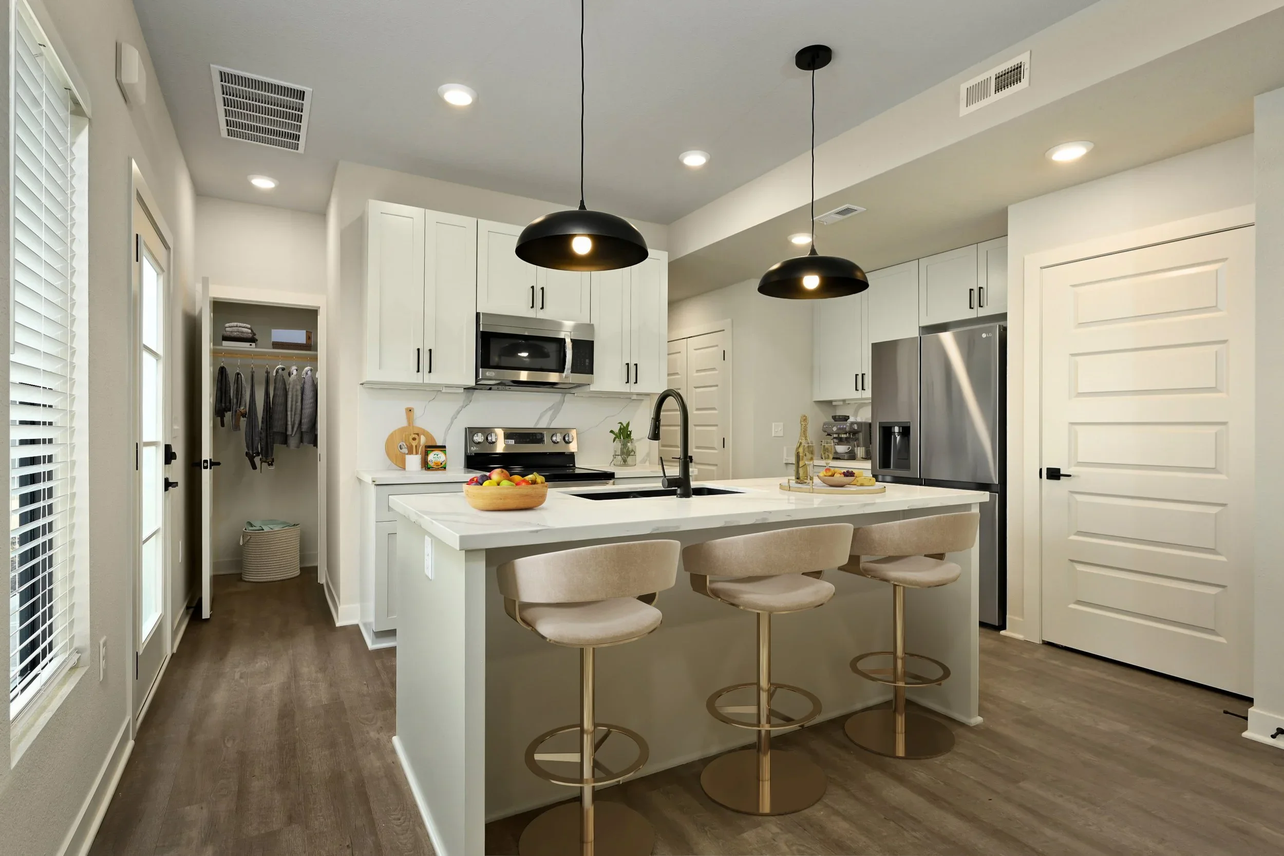 Modern kitchen with white cabinets, stainless steel appliances, a kitchen island with beige bar stools, and pendant lighting.