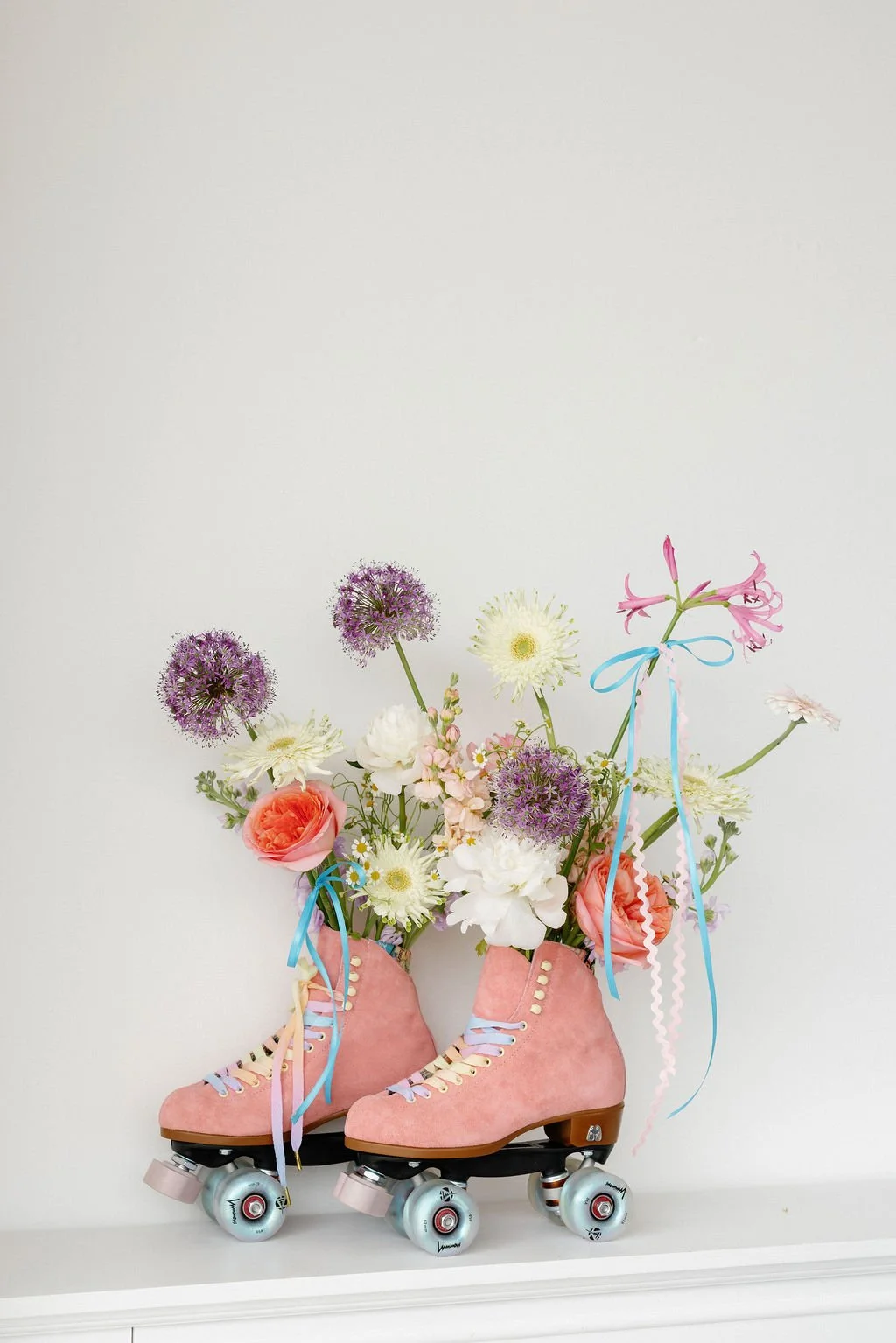 Pink roller skates filled with colorful flowers, including purple, white, and pink blossoms, tied with blue and pink ribbons.