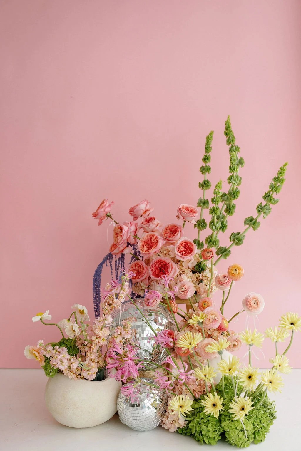 Colorful flower arrangement in vases with pink, yellow, and green flowers against a pink background.