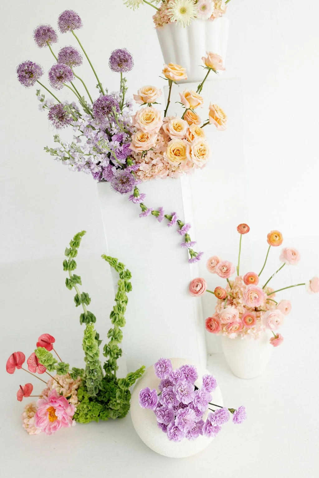 Arrangement of various colorful flowers in white vases against a white background.