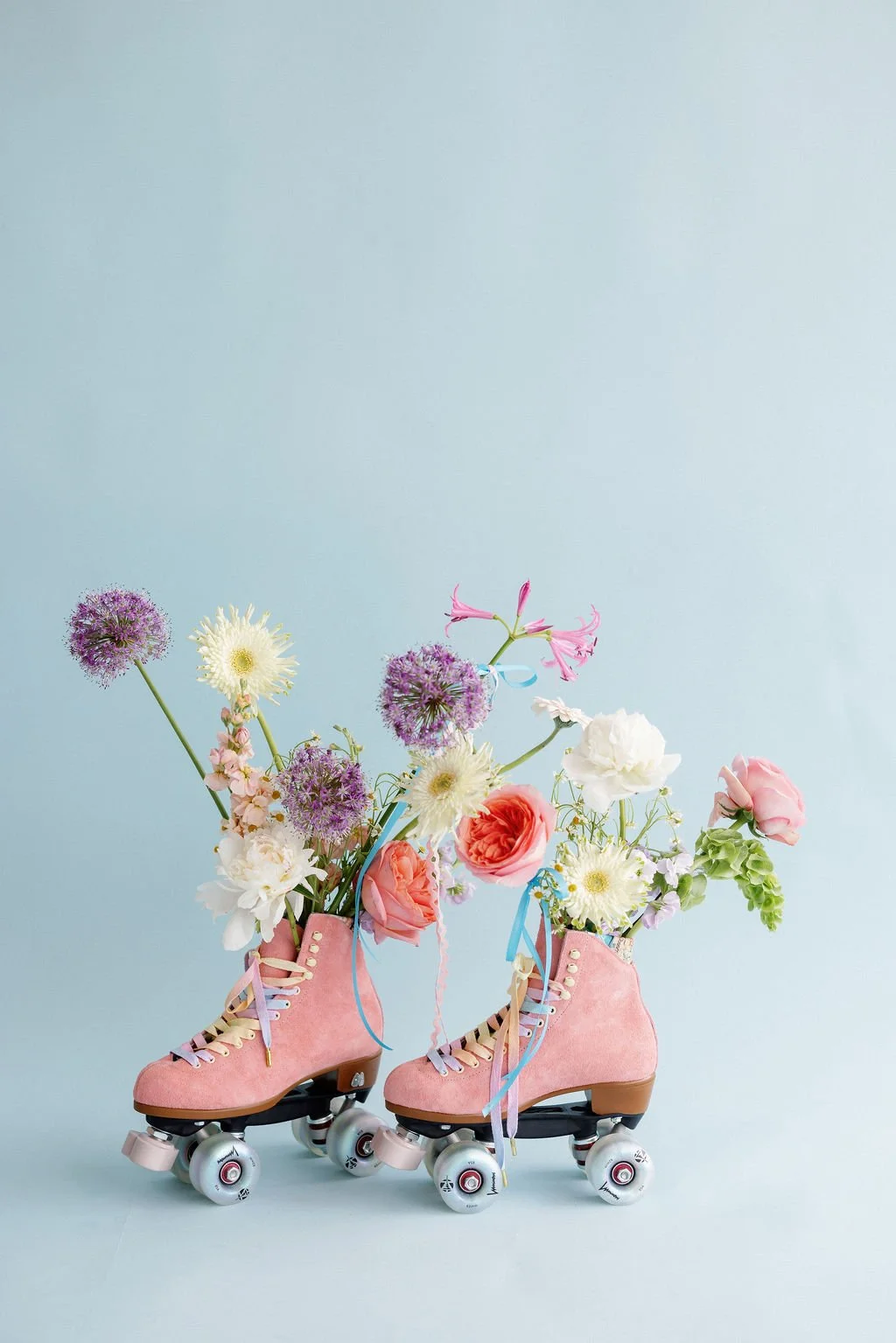 Pink roller skates with flowers inside, set against a light blue background.