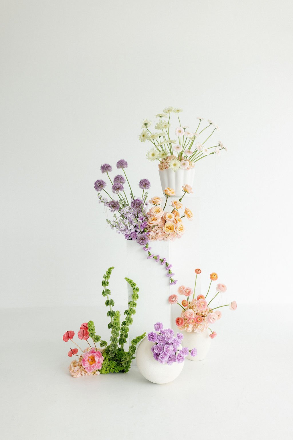 Arrangement of various colorful flowers in white vases against a plain white background.