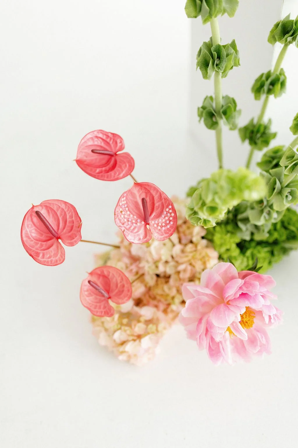 Arrangement of pink, peach, and green flowers with pale pink anthuriums and greenery in a white vase.