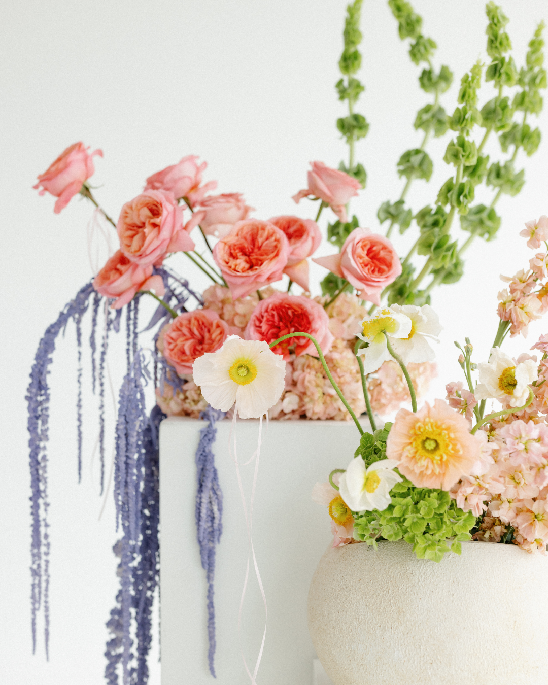 Arrangement of pink, peach, white, and green flowers in vases with a plain white background.