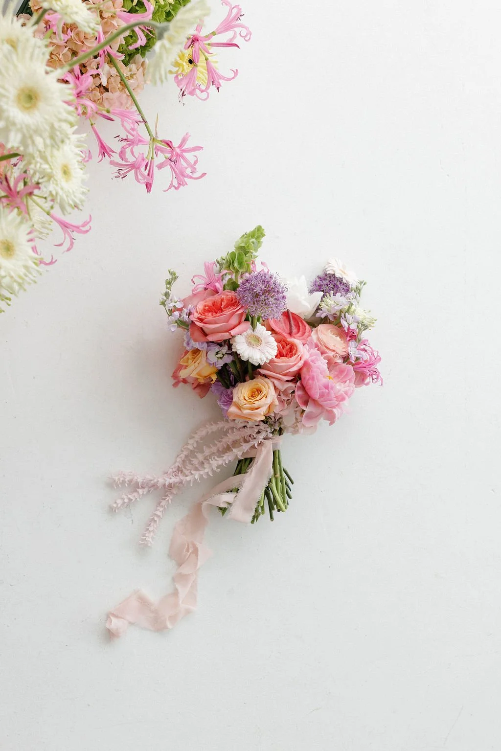 A small bouquet of pink, white, and purple flowers tied with a pink ribbon on a white background.