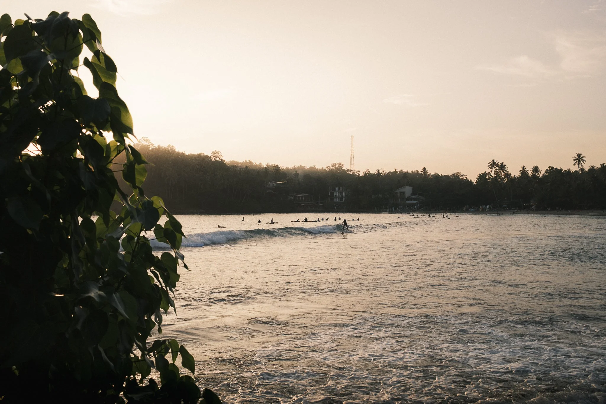 View of Hiriketiya Beach with surfers catching waves at sunset