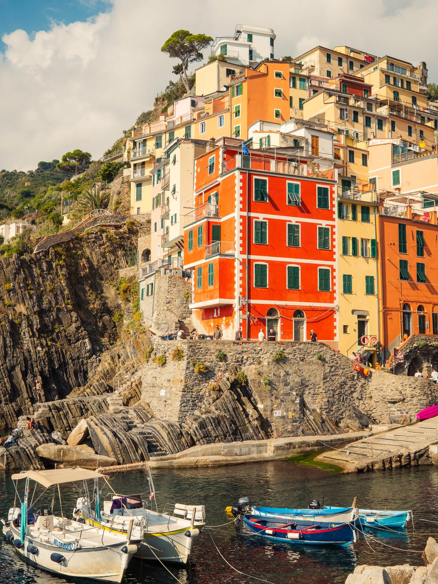Colorful buildings along a rocky hillside overlooking a marina with small boats in the water.