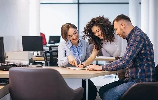 Three colleagues working together around a table in an office.