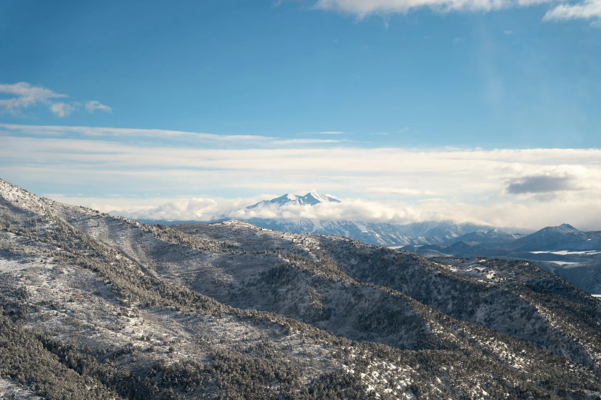 Snow-covered mountains and hills under a partly cloudy blue sky.