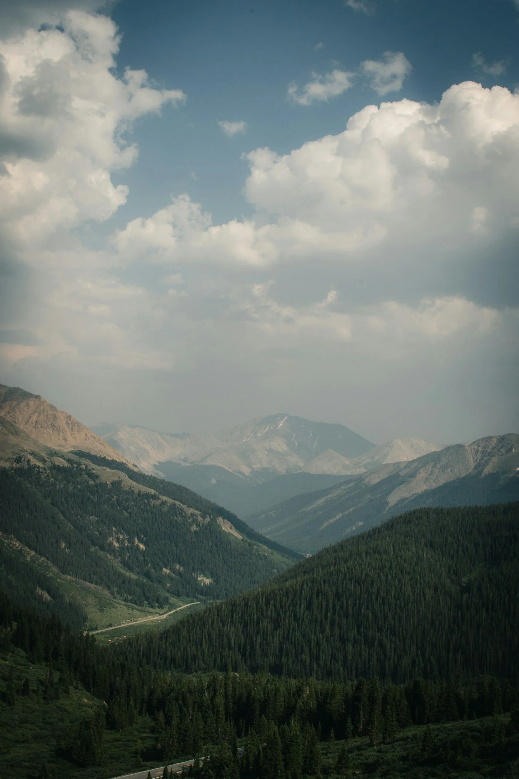 Mountain range under a partly cloudy sky with valleys and dense evergreen forests.