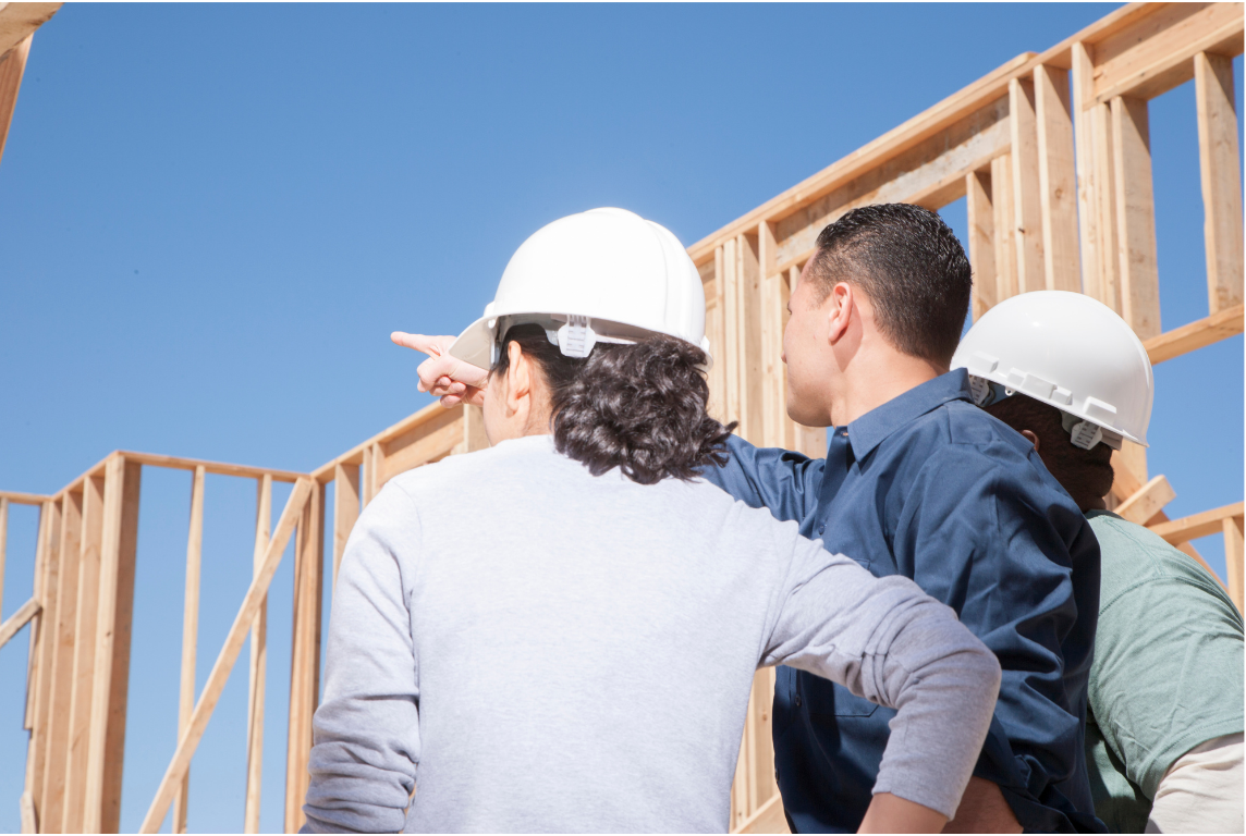 Construction team at a building site, discussing a wall framing layout of a new addition.