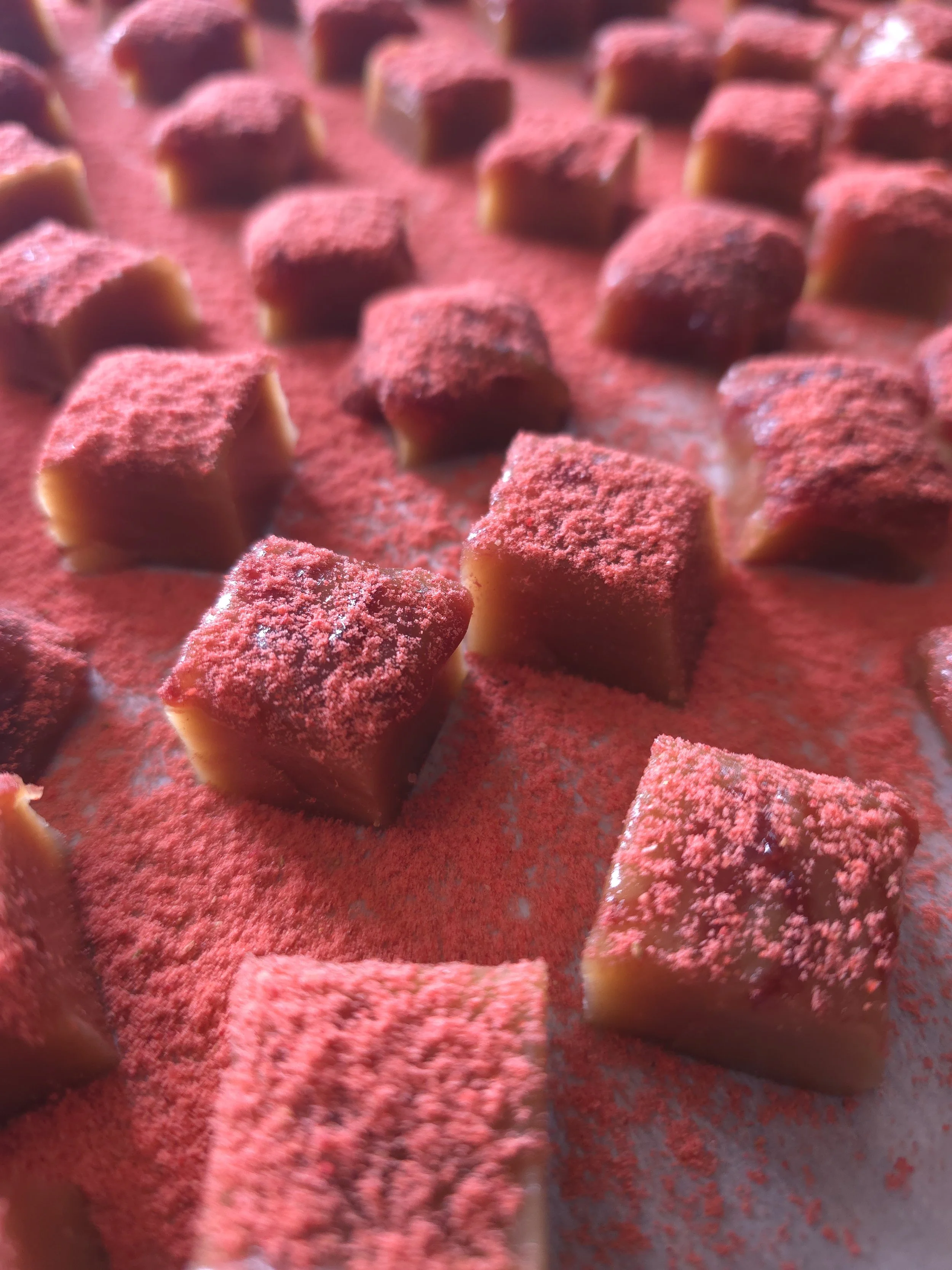 Close-up of small, cube-shaped chocolates coated with red powder on a surface.