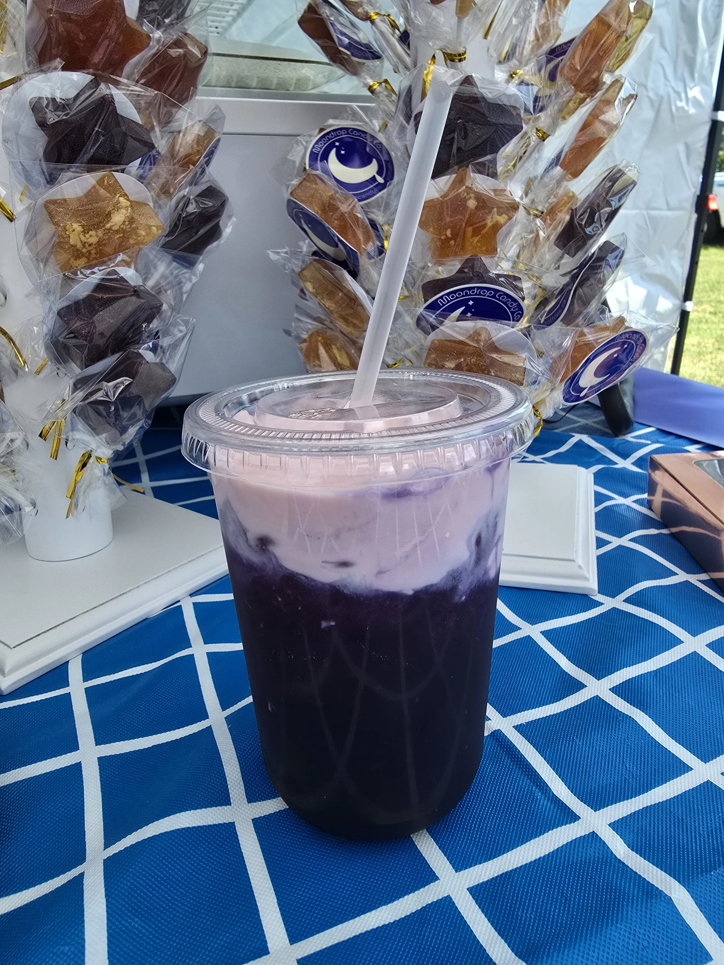A plastic cup filled with a purple-colored beverage with ice, placed on a blue and white checkered tablecloth.
