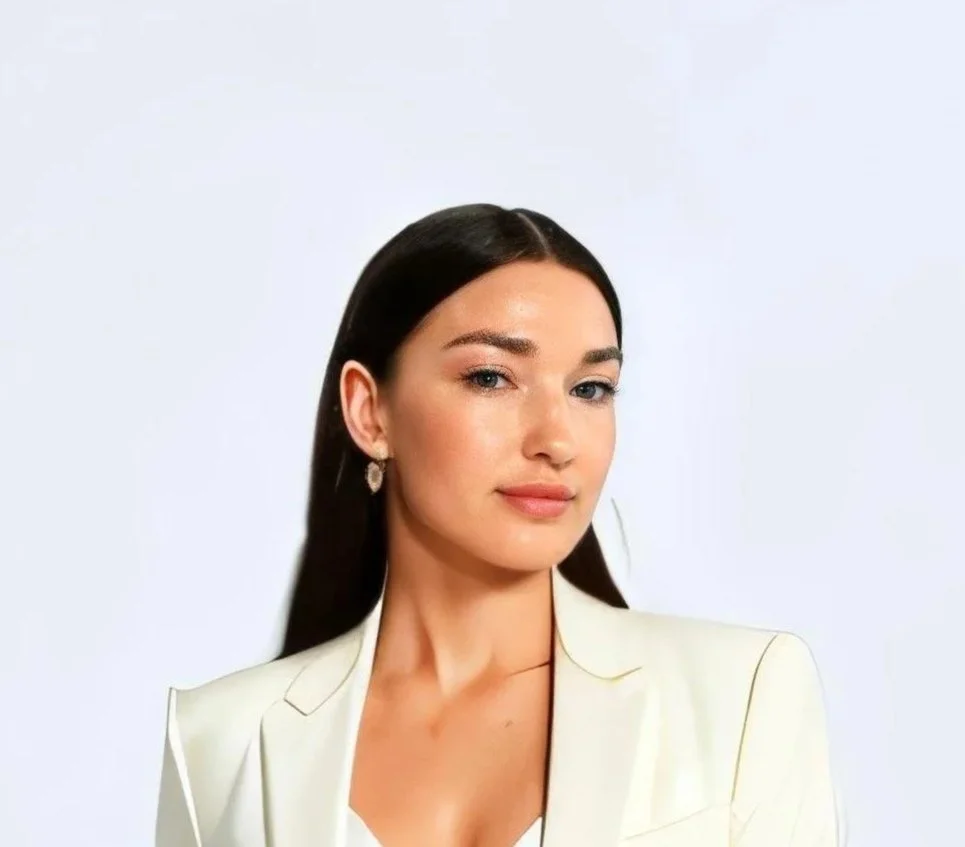 Portrait of a woman with long dark hair, wearing a light-colored blazer, against a plain background.