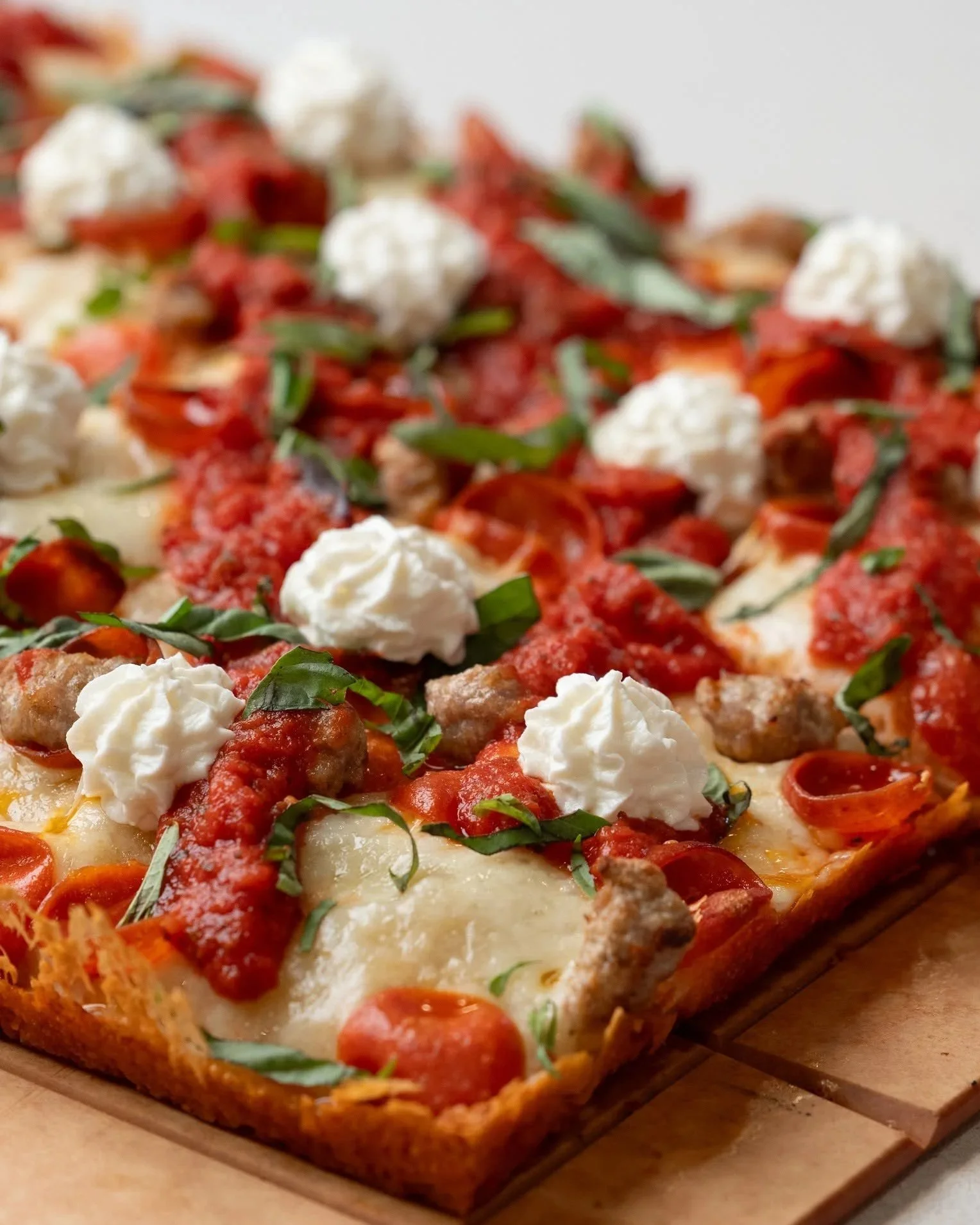 Close-up of a freshly baked pizza topped with pepperoni, sausage, mozzarella cheese, tomato sauce, and fresh basil on a wooden pizza board.
