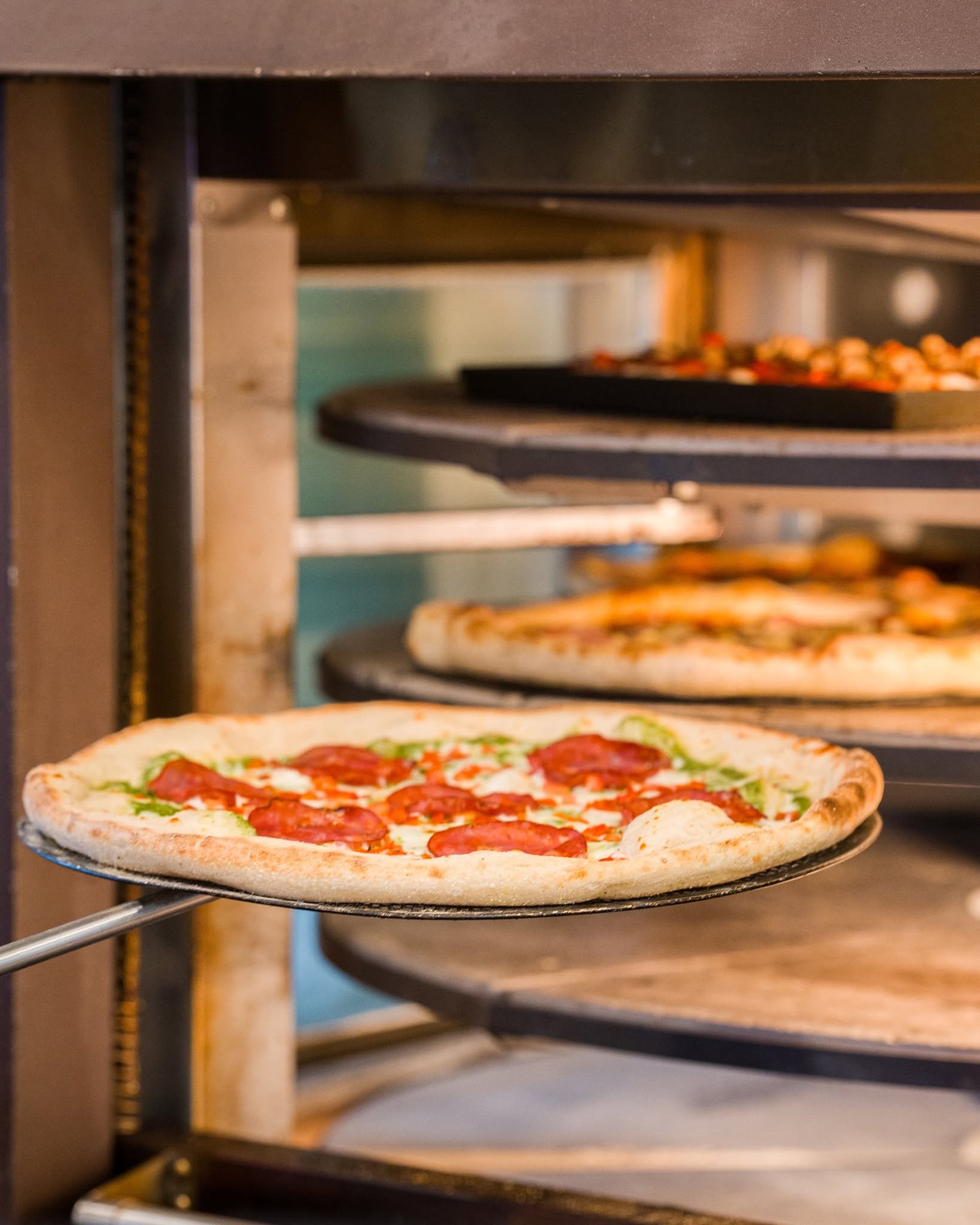 A pizza with pepperoni, green peppers, and cheese being taken out of an oven on a pizza peel.