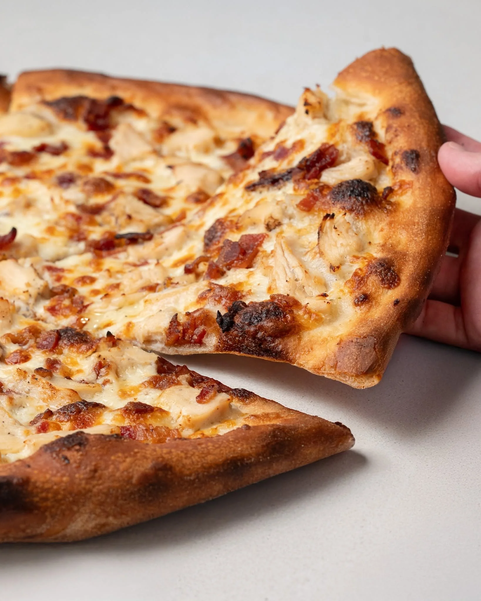 Close-up of a hand holding a slice of pepperoni pizza with cheese and toppings, on a white surface.