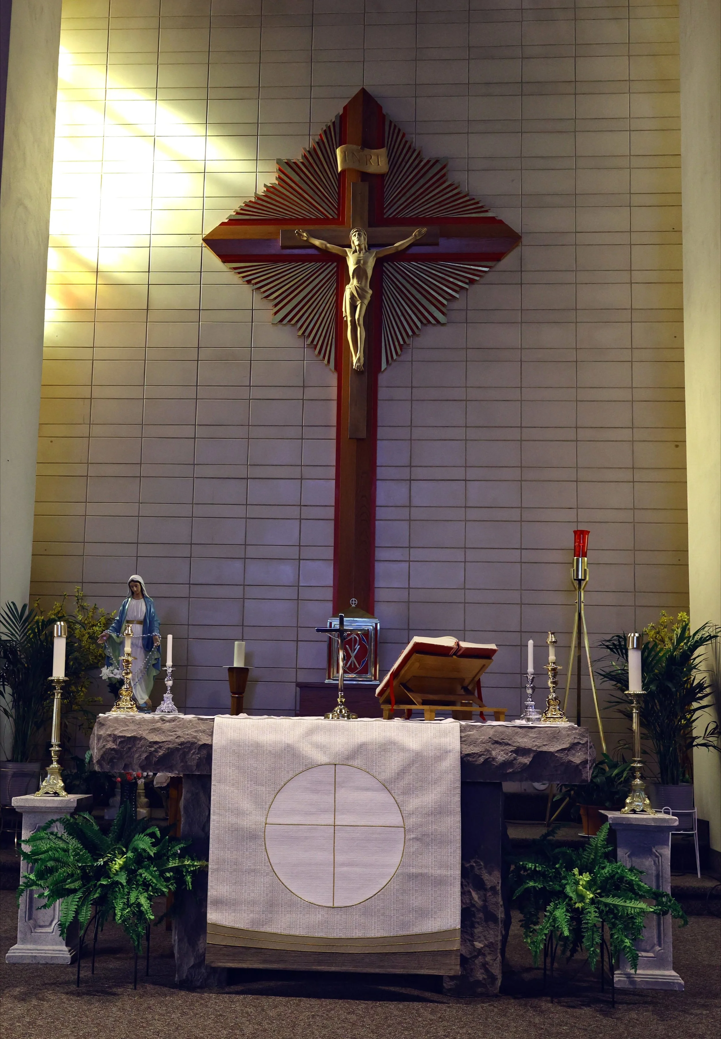 Religious altar with crucifix, statue of Virgin Mary, candles, and greenery, set against a tiled wall in Sanctuary of St Thomas Aquinas Roman Catholic Church in St Catharines Ontario.