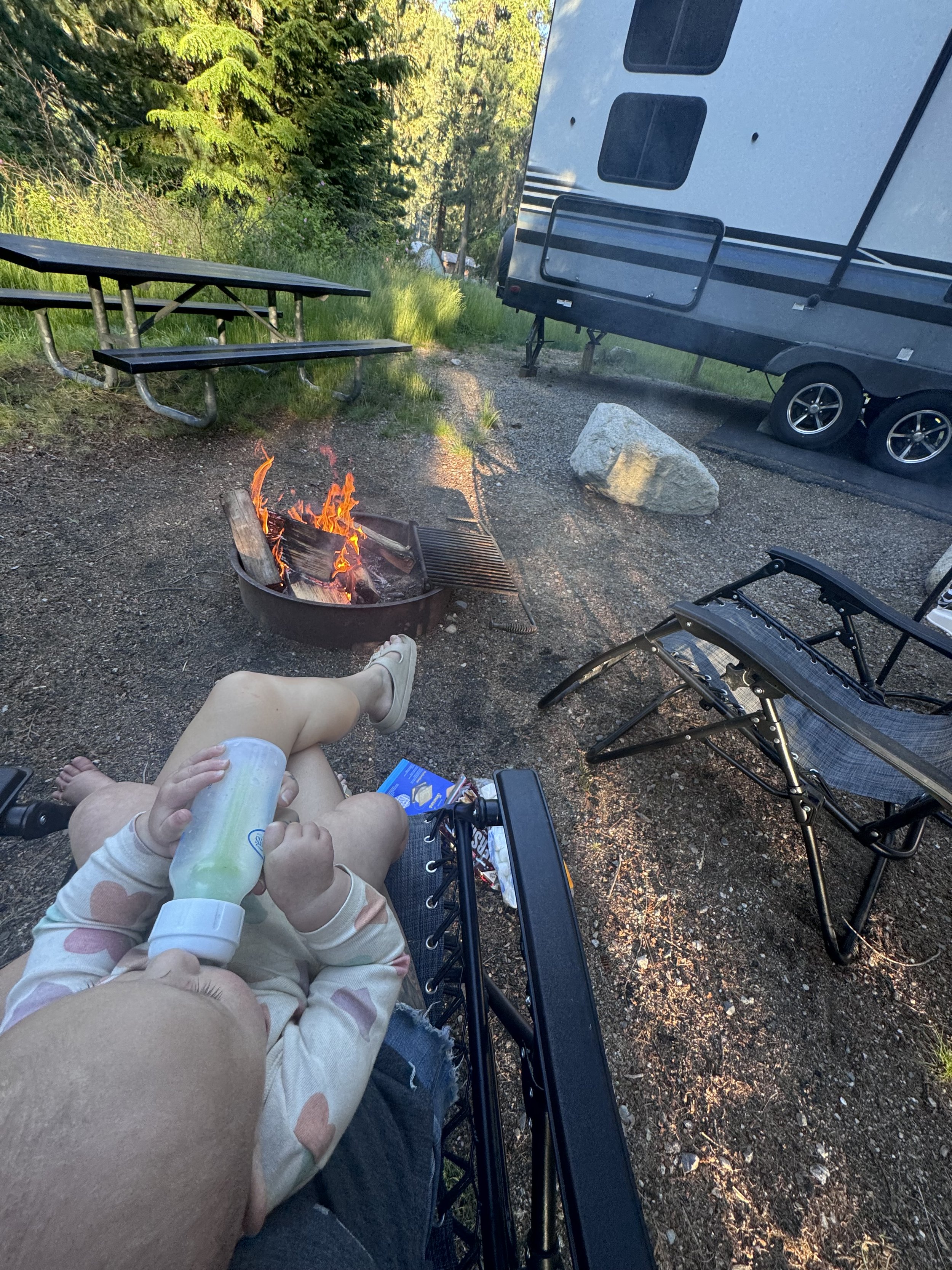 Baby holding bottle in camp chair next to a fire