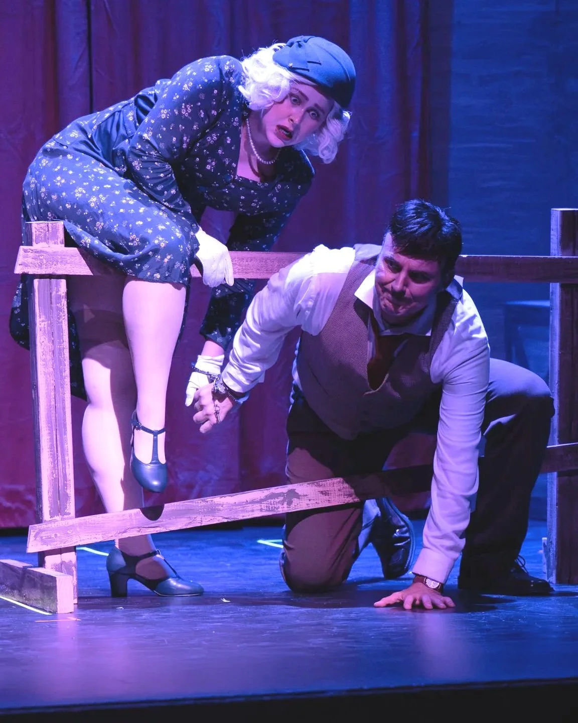 Two actors on stage, one woman dressed in vintage clothing and a woman in a business casual outfit, engaging in a theatrical performance.