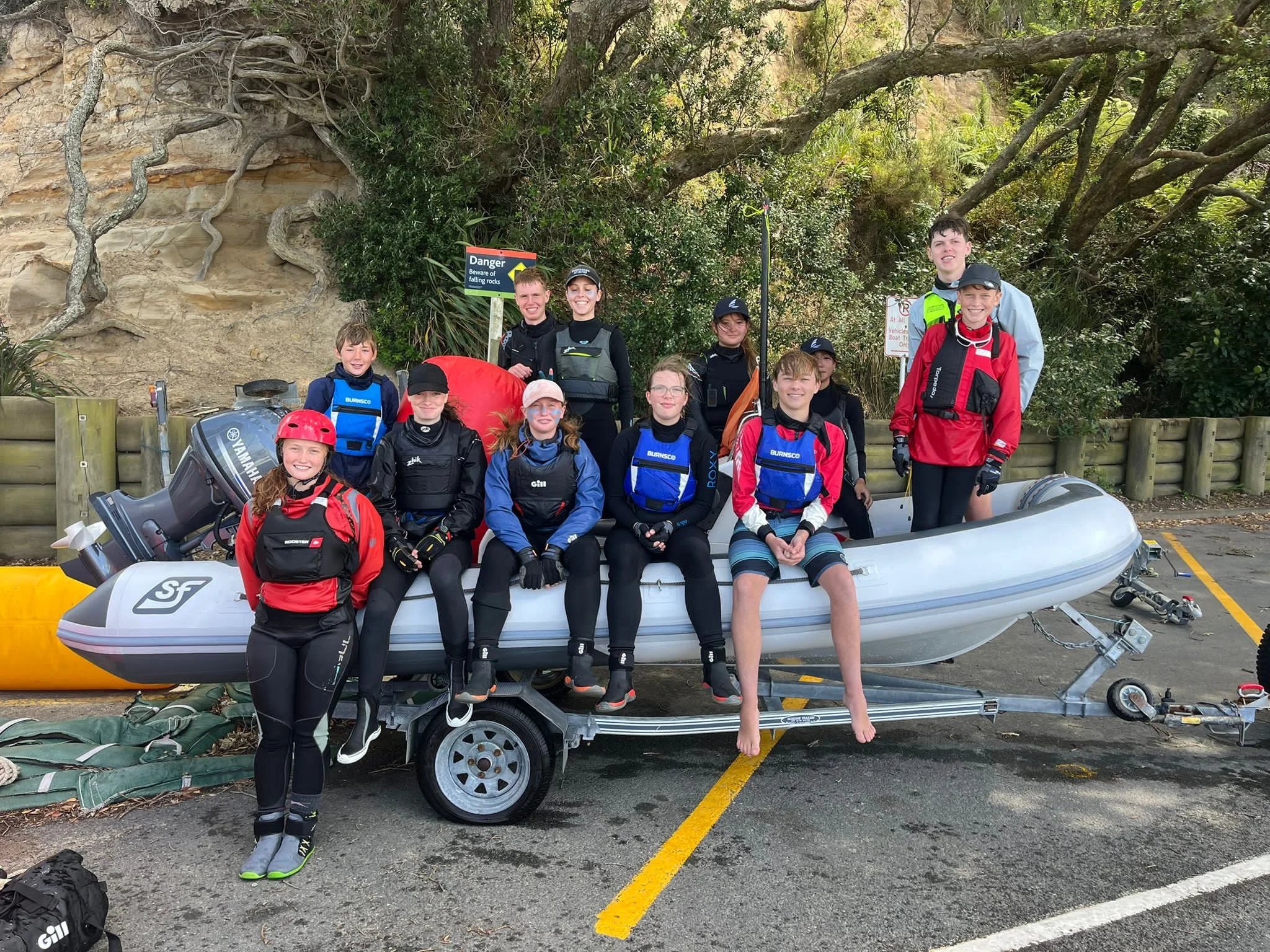 A group of NBYC young sailors in wetsuits and lifejackets with a club rescue boat at Birkenhead Wharf