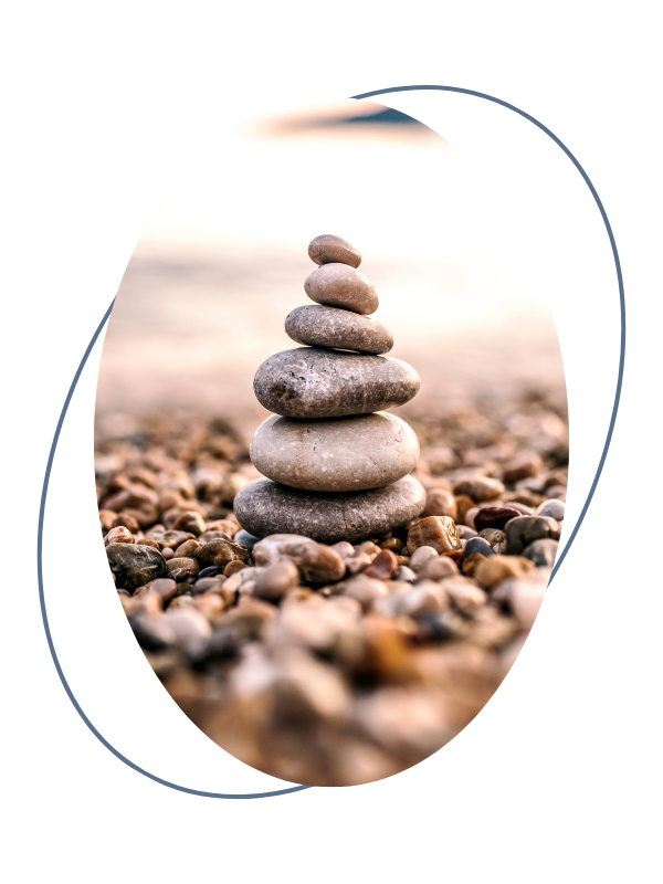 Stack of smooth, rounded stones balanced on top of each other on a pebble beach with soft blurred background.