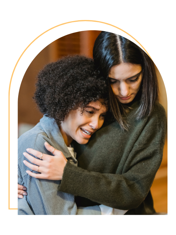 Two women hugging each other, one with curly hair and the other with straight dark hair, in a warm embrace.