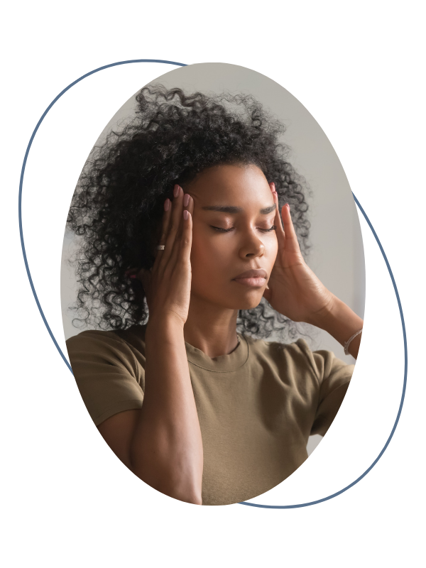 A woman with curly hair is pressing her hands against her temples with her eyes closed, appearing to experience stress or frustration.