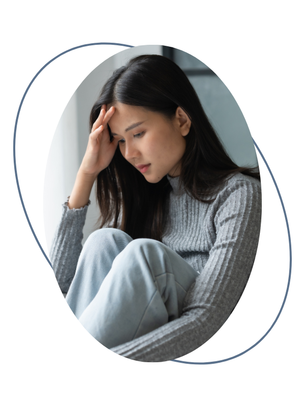 A young woman sitting with her knees drawn up, holding her head with one hand, appearing distressed or deep in thought.