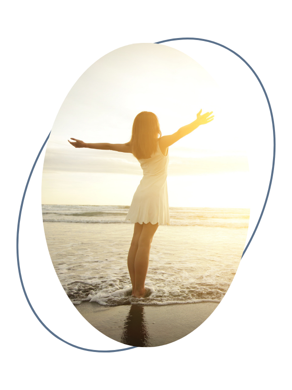 A woman standing on a beach with arms outstretched during sunset
