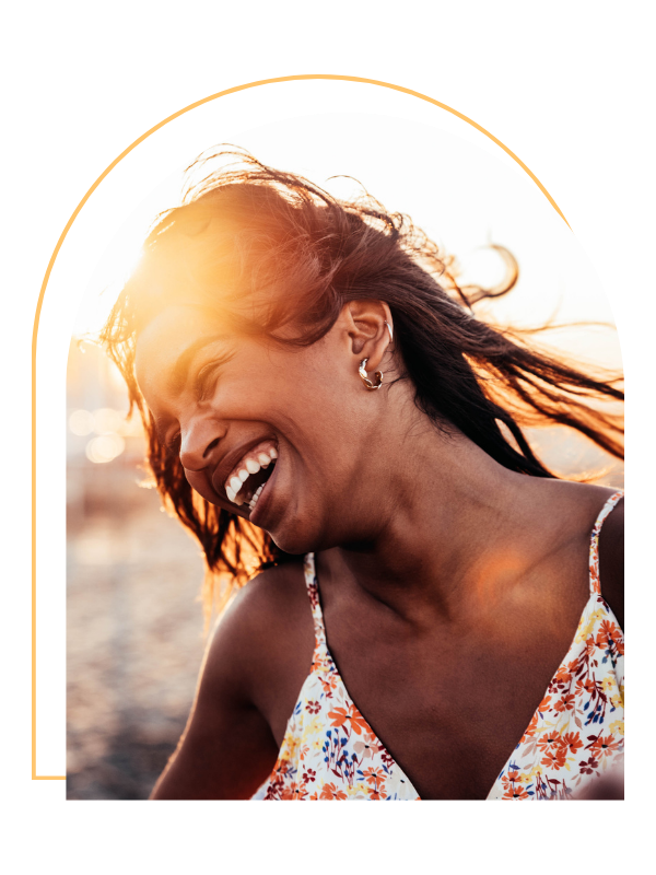 A woman with dark hair laughing outdoors during sunset.
