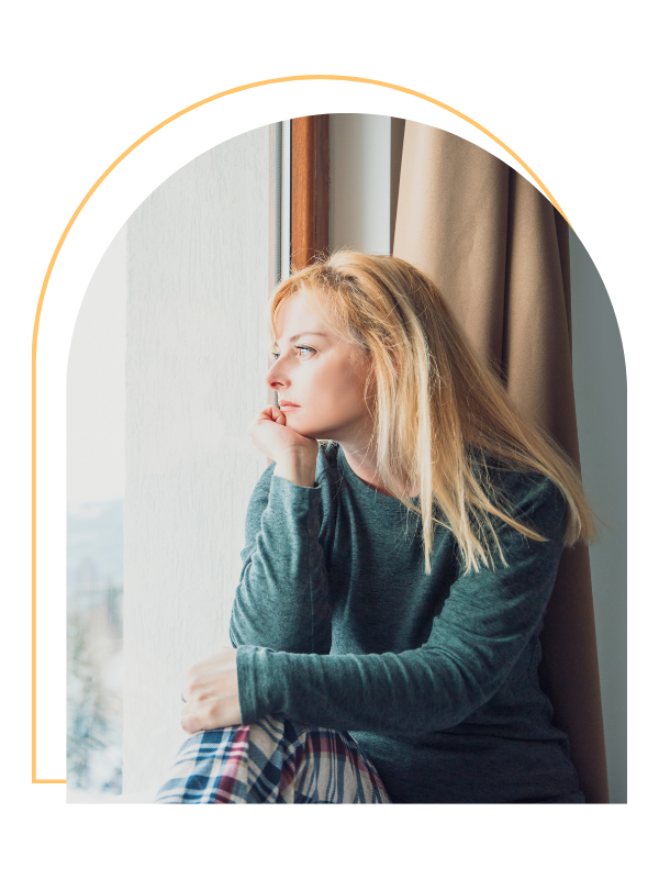 A woman with blonde hair sitting by a window, gazing outside thoughtfully.