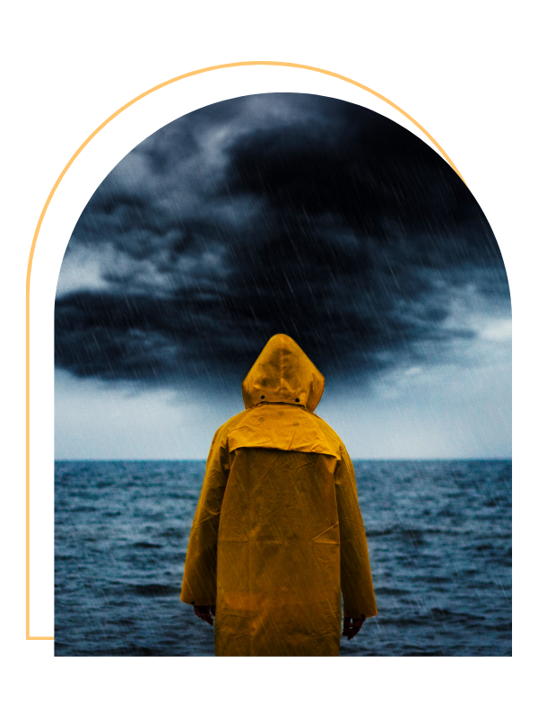 Person in yellow raincoat standing on a boat or dock facing stormy ocean and dark, stormy sky with rain.