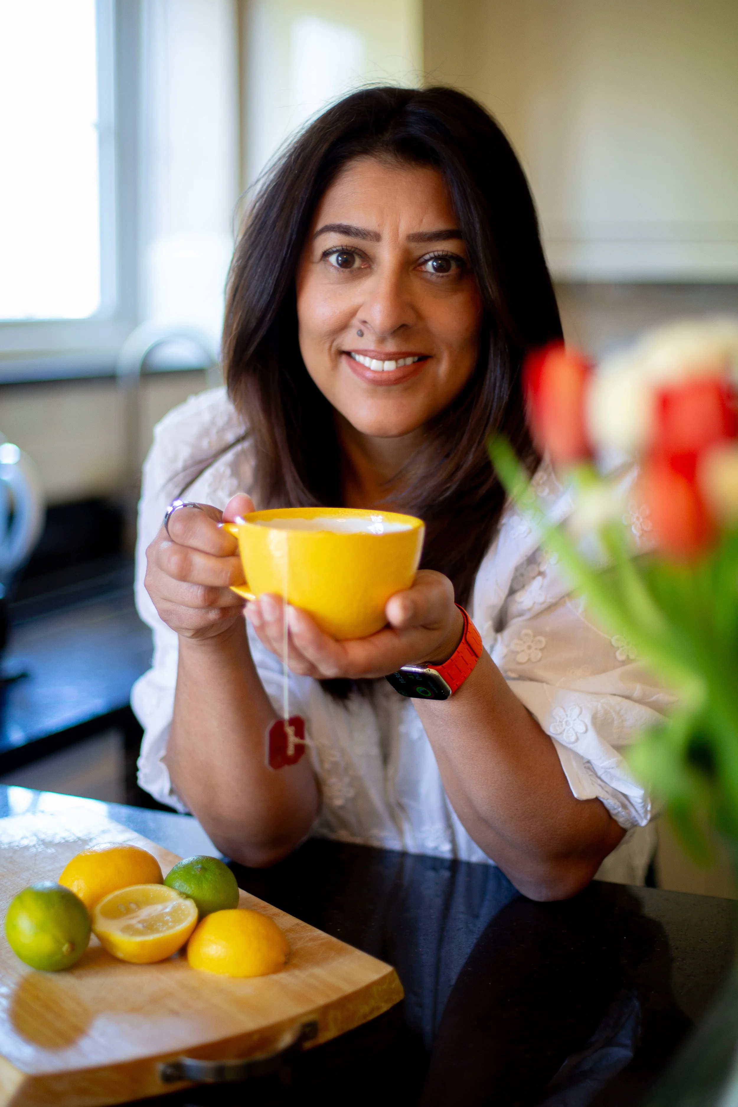 Image of health coach in kitchen, smiling and holding a cup of tea and looking at camera