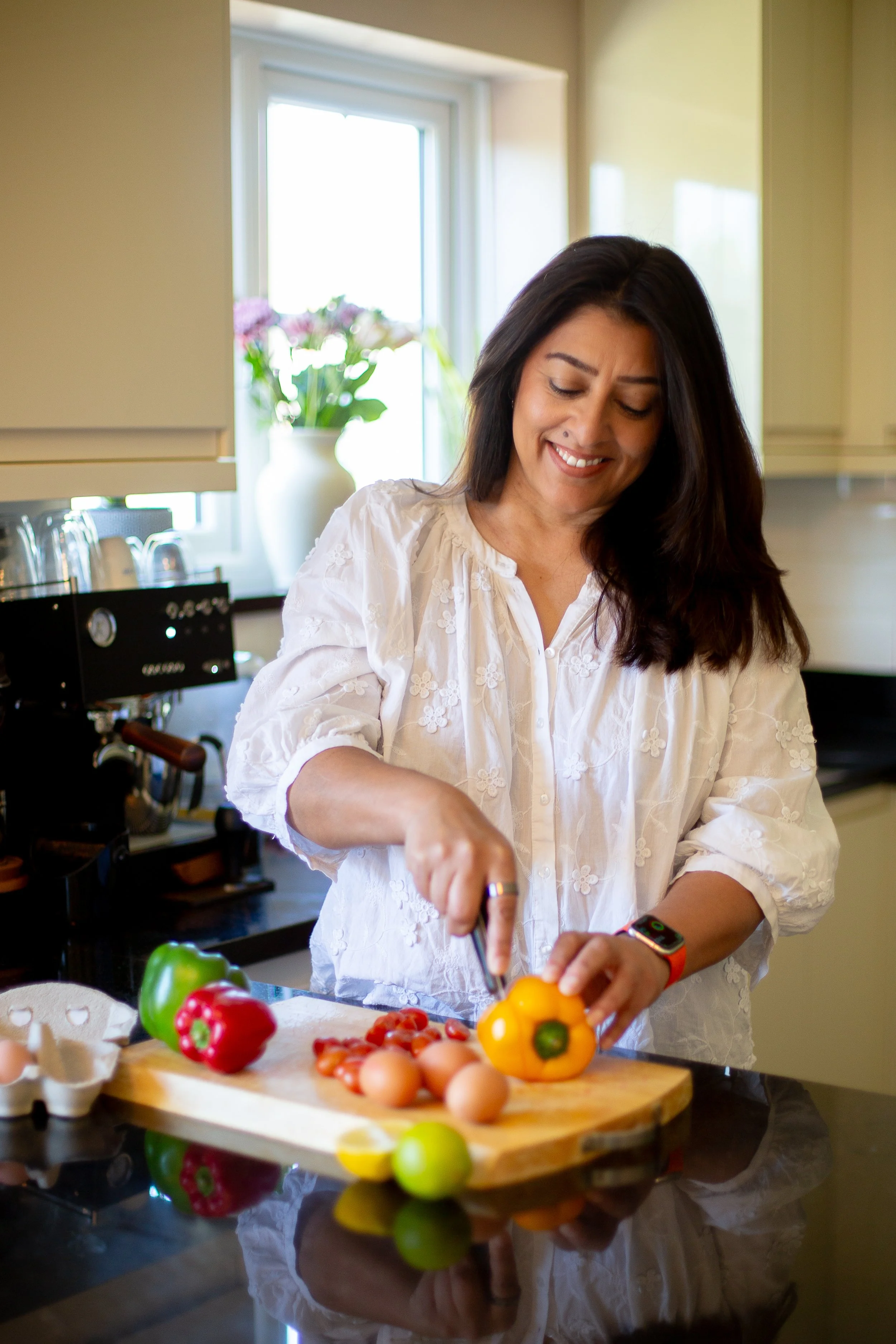 Image of health coach in kitchen looking down and smiling whilst chopping peppers