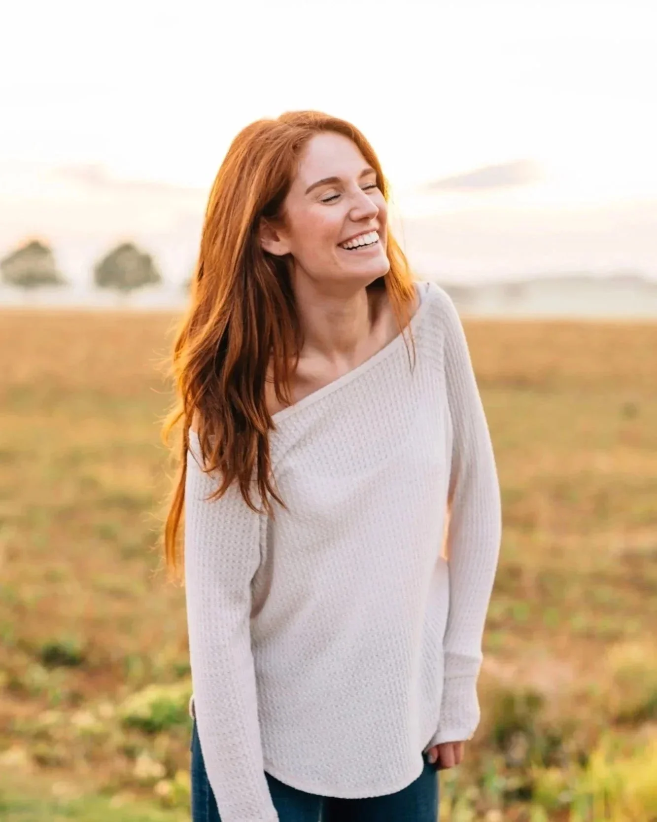 Image of woman in midlife smiling and laughing whilst standing in a field outdoors