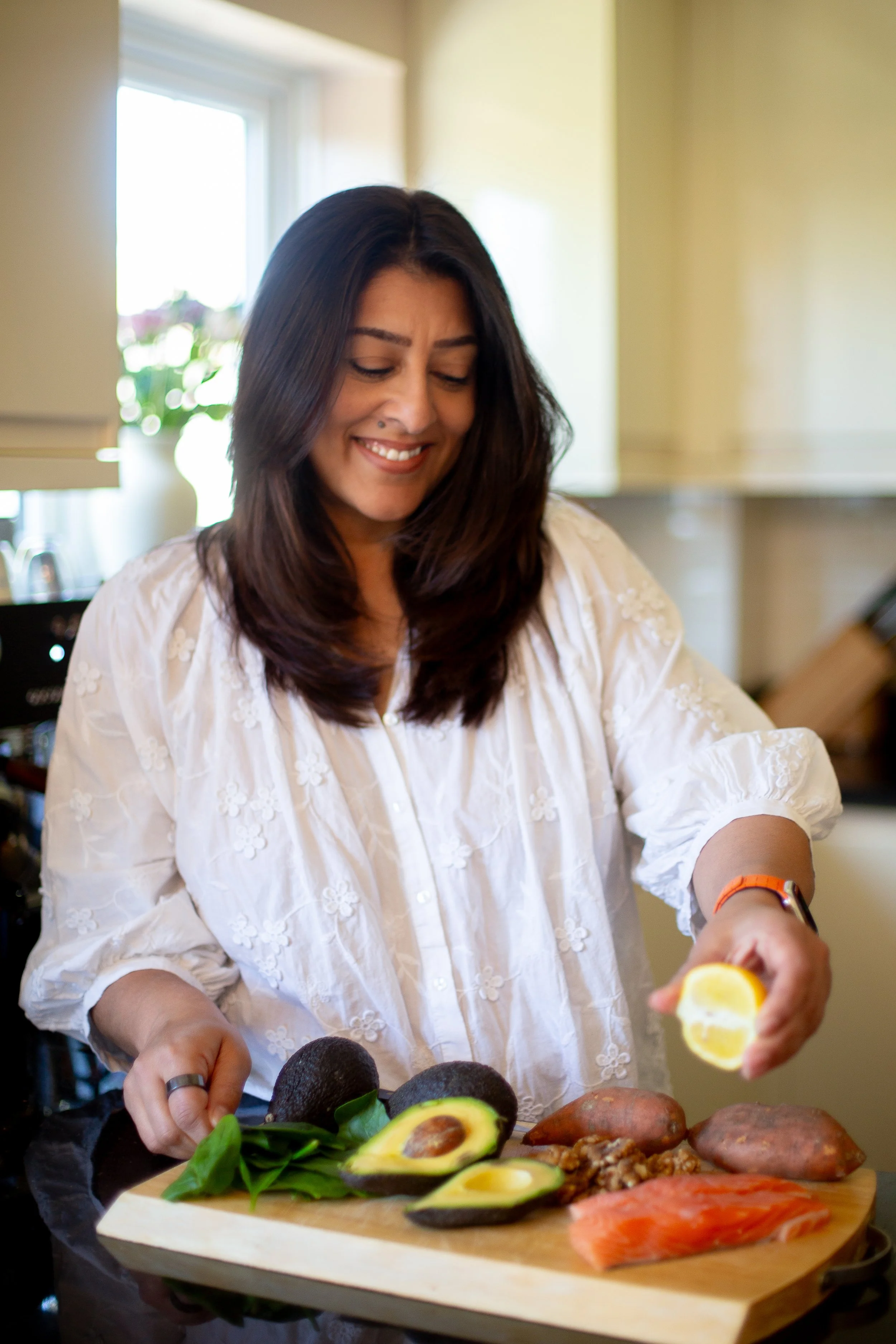 Image of health coach in kitchen looking down and smiling whilst squeezing lemon onto salmon